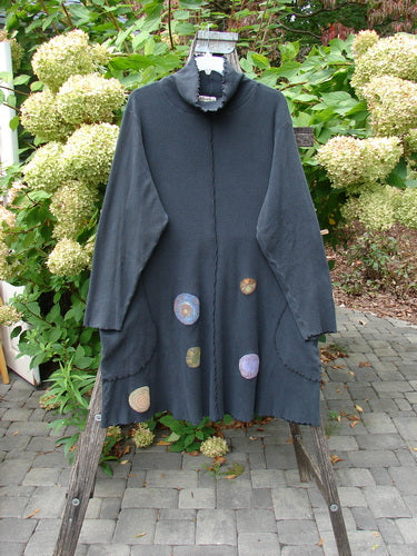 Barclay Patched Thermal Exterior Stitch Side Pocket Tunic Off Black Size 2 displayed on a wooden stand outdoors, showcasing its A-line cut, long sleeves, and colorful appliqué patches on the front.