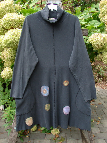 Barclay Patched Thermal Exterior Stitch Side Pocket Tunic Off Black Size 2, featuring raw-edge seams, funnel collar, long sleeves, pastel appliqué patches, and drop pockets, hanging on a bench outdoors.