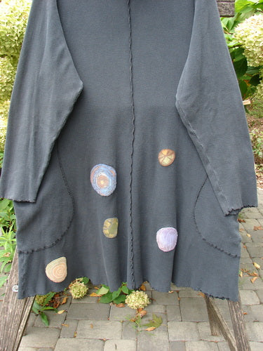 Barclay Patched Thermal Exterior Stitch Side Pocket Tunic Off Black Size 2, a cozy open-front design with whimsical pastel patches, draped over a wooden bench outdoors, highlighting its unique artistic flair.