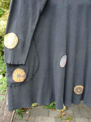 Barclay Patched Thermal Exterior Stitch Side Pocket Tunic in Off Black drapes over a bench, showcasing multicolored appliqué patches and curly-edged details, reflecting unique Bluefishfinder.com creativity.