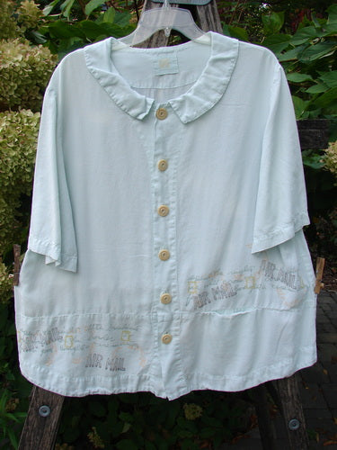 2000 Tencel Camp Shirt Airmail Shark Size 0, featuring a ruffled collar, oversized wooden buttons, and travel-themed print. This loose, flowing chambray top offers a unique, vintage-inspired style.