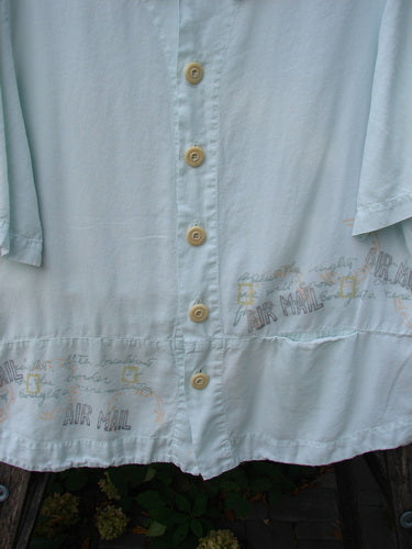 2000 Tencel Camp Shirt Airmail Shark Size 0: Light-blue short-sleeved blouse with cream buttons, Peter Pan collar, front drop pocket, and airmail print along hem, reflecting Bluefishfinder's vintage, creative style.