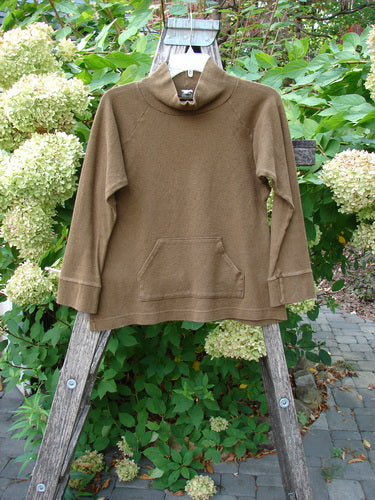 2000 Wool Funnel Neck Raglan Top Unpainted Pebble Smaller Size 1 displayed on a wooden ladder outdoors, showcasing its loose funnel neck, low-set kangaroo pocket, and banded cuffs, reflecting vintage Blue Fish Clothing style.