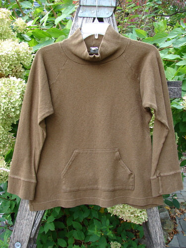 2000 Wool Funnel Neck Raglan Top Unpainted Pebble Smaller Size 1, featuring a high neck, long sleeves, kangaroo pocket, and banded cuffs, displayed on a hanger against a natural backdrop.