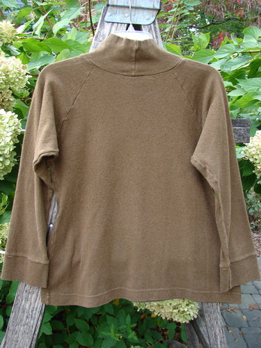 Back view of the 2000 Wool Funnel Neck Raglan Top Unpainted Pebble Smaller Size 1, featuring a relaxed half-height turtleneck and banded cuffs, elegantly draped over a wooden trellis.
