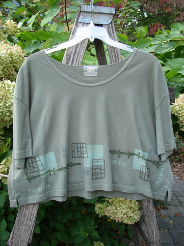 2000 City Side Crop Tee Top Navigation Border Park Size 2 features a boxy, short-sleeved crop-top with a graphic hem, draped on a rustic ladder, showcasing Blue Fish Clothing’s unique style and craftsmanship.