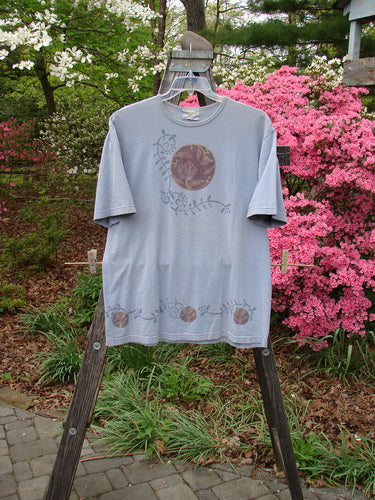 1999 Short Sleeved Tee Floral Medallion Bluestone Size 1 hanging on a swinger in front of a pink flowered bush, showcasing a thinner slightly rolled ribbed neckline and signature Blue Fish patch.