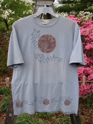 1999 Short Sleeved Tee Floral Medallion Bluestone Size 1 displayed on a hanger, showcasing a floral design and slightly rolled ribbed neckline, highlighting its vintage style and organic cotton fabric.