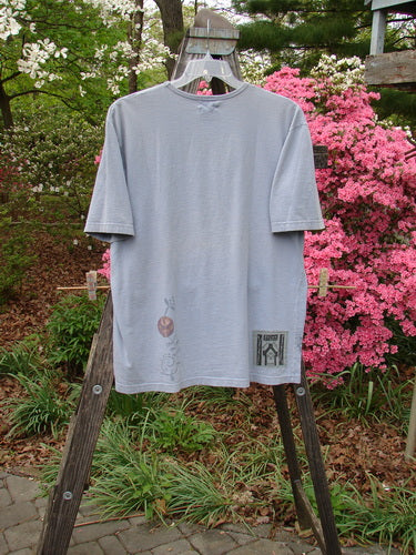 1999 Short Sleeved Tee Floral Medallion Bluestone Size 1 displayed on a wooden hanger outdoors, showcasing its ribbed neckline and super floral medallion theme paint, emphasizing its vintage charm.