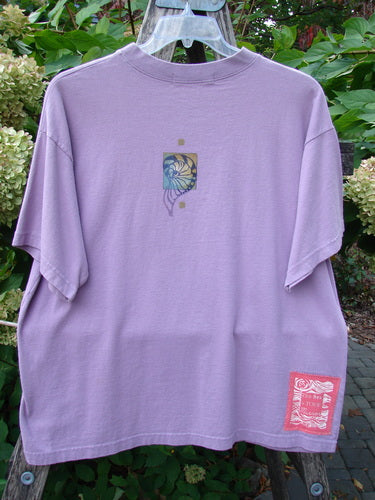 1997 Short Sleeved Tee Five Shell Jasmine Size 1 in lavender-purple with a square abstract floral design on the back and a red label near the hem, hanging outdoors on a garden trellis.