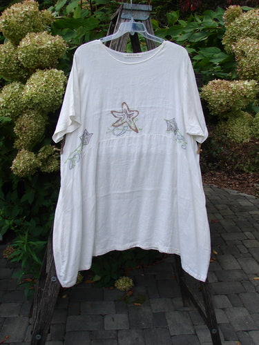 1997 Urchin Dress Sealife Froth Size 2, featuring three starfish motifs embroidered on a loose-fitting white tunic, displayed outdoors against hydrangeas on a wooden ladder.