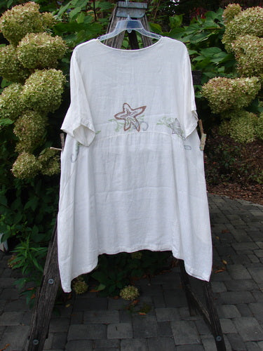 1997 Urchin Dress Sealife Froth Size 2, displayed on a wooden ladder, features lightweight linen, starfish embroidery, and a unique hemline, epitomizing BlueFishFinder's vintage, expressive style.