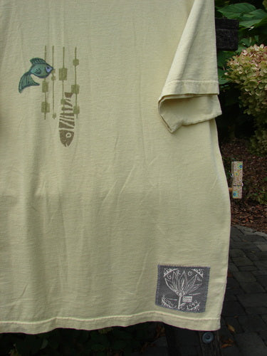 1999 Short Sleeved Tee Single Fish Citron Size 1, featuring a stylized fish print and Blue Fish patch, draped over a railing, showcasing its unique boxed shape and drop shoulders.