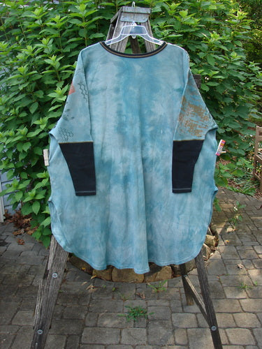 Barclay Thermal Contrast Revival Top Farm Turq OSFA displayed on a wooden chair, showcasing its distinctive black sleeves, ribbed neckline, and unique farm-themed design with a flowing silhouette.
