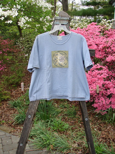 1999 Patched Short Sleeved Crop Tee Floral Medallion Bluestone Size 1 displayed on a wooden easel, showcasing a detailed flower design on the front.