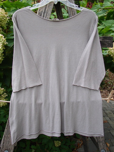 Barclay Batiste Raw Edge Layering Top Unpainted Stone Size 1 hangs on a wooden ladder, showcasing its loose fit, three-quarter sleeves, wider raw-cut neckline, and rolled edgings, embodying BlueFishFinder's vintage charm.