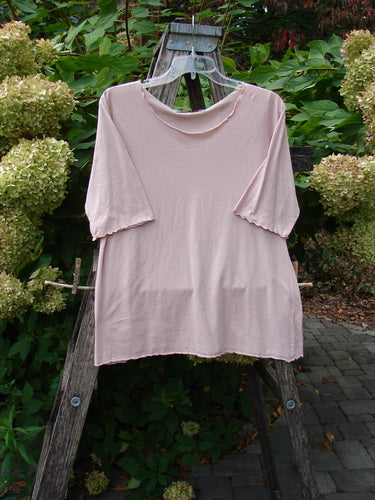 Barclay Batiste Curl Edge Layer Top Unpainted Blush Size 1, draped over a rustic wooden ladder, showcasing its curly neckline, hem, and sleeves, set against a garden backdrop with hydrangeas.