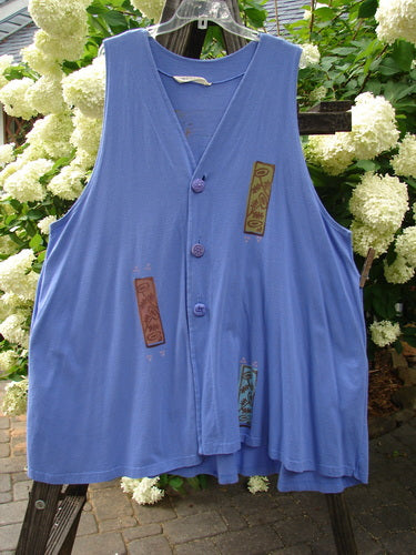 1997 Simple Vest Flower Sprig Skylark Size 2: A blue vest with patches, buttons, and a sweet flower sprig patch on the lower back. Features include swing style, scooped hemline, deep side pockets, and oversized knotted textured buttons. Made from organic cotton.