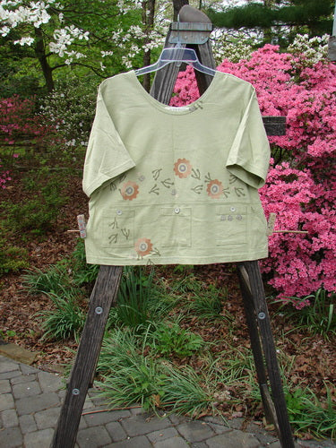 Vintage 1996 Collector's Top with Floral Seedling Design, Size 2, featuring a green shirt with flower patterns on a wooden easel. Unique details include a wider neckline, A-line flare, and floral pockets with original paper buttons. From BlueFishFinder specializing in Vintage Blue Fish Clothing.