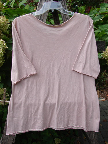 Barclay Batiste Curl Edge Layer Top Unpainted Blush Size 1, featuring a scooped neckline, elbow-length curly edged sleeves, and a straight hem, displayed against lush foliage. Perfect for mixing with other Blue Fish pieces.