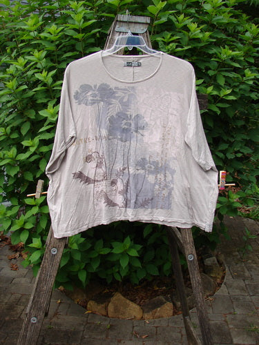 Barclay Cotton Slub Cricket Cap Sleeve Tee Poppy Garden Mist OSFA displayed on a swinger, showcasing its cap sleeves, boxy shape, and seamless design. The organic cotton tee features a unique poppy garden theme.