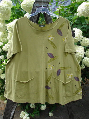 Barclay Double Pocket Twinkle Top Finch Leaf Peapod Size 2: A green shirt with a bird design, featuring a ruffle hem, banded lower sleeves, and double drop pockets. Made from organic cotton, this top has a softly rounded neckline and an A-line shape.