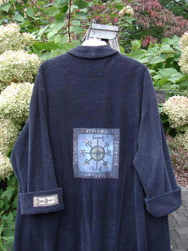 1999 Patched Chenille Angle Pocket Jacket Holiday Black Size 1 displayed on a hanger, showcasing a large compass-themed patch on the back and a smaller patch on the sleeve, amidst hydrangea blooms.