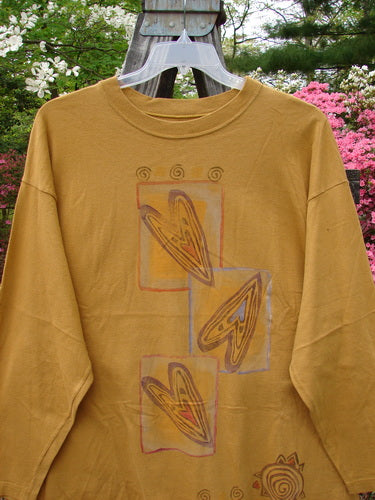 1996 Long Sleeved Tee Falling Heart Old Gold Size 2: A yellow shirt with a heart design, dropped shoulder, ribbed neckline, and Blue Fish patch. Vintage Blue Fish Clothing from BlueFishFinder.com.