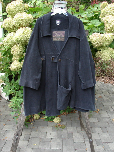 2000 Celtic Moss Highlander Coat Unpainted Black Size 1 displayed outdoors, showcasing its oversized, draped cut, wide sleeves, patch pockets, and oversized front buttons, hanging stylishly against a natural backdrop.