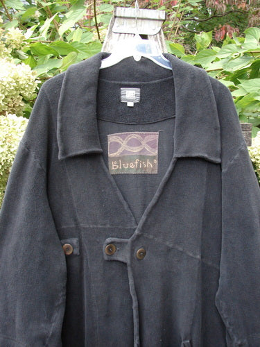 2000 Celtic Moss Highlander Coat Unpainted Black Size 1 featuring a wide shawl-style collar, two large buttons, and intricate seam detailing, hanging outdoors on a plastic hanger against foliage.