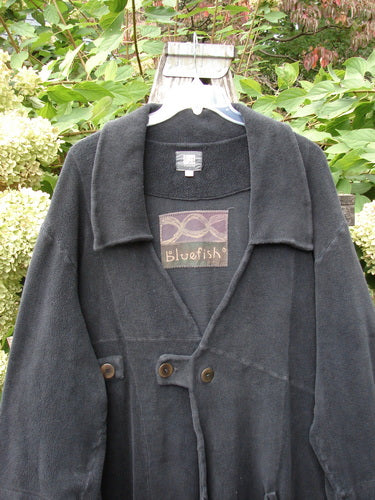 2000 Celtic Moss Highlander Coat Unpainted Black Size 1, featuring a loose shawl-style collar and double-button closure, hanging outdoors against leafy shrubs, showcasing its plush, dense winter weight and empire waistline design.