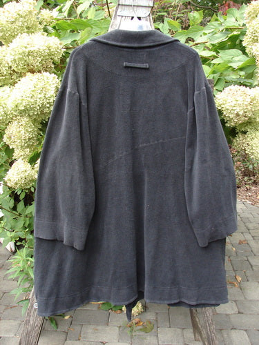 Back view of the 2000 Celtic Moss Highlander Coat Unpainted Black Size 1, hanging on an outdoor trellis. The coat features dense fabric with unique diagonal seams and oversized buttons, embodying Bluefishfinder.com's vintage style.