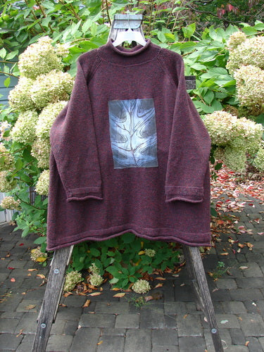 1998 Patched Alpaca Roll Neck Raglan Sweater Wineberry Tweed OSFA features a heathered burgundy tunic with a mock neck, dropped shoulders, and a blue-gray botanical patch on the front.