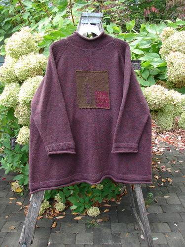 1998 Patched Alpaca Roll Neck Raglan Sweater in Wineberry Tweed OSFA, displayed on a wooden stand, features a square tree appliqué, ribbed collar, and oversized A-line shape in a garden setting.