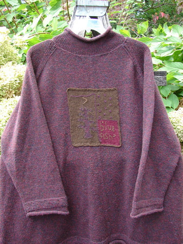 1998 Patched Alpaca Roll Neck Raglan Sweater Wineberry Tweed OSFA with a two-tone felt patch, showcasing a stylized plant motif, hangs outdoors, highlighting its loose fit and textured marled alpaca wool.