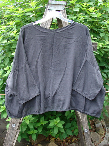 Barclay Twill Atmosphere Overlayer Boxy Top Unpainted Black OSFA hangs from a clothes rack, showcasing its lightweight, flowy design with a rounded neckline and three-quarter length dolman sleeves.