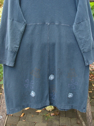 1999 Thermal Home Dress Paisley Peacock Size 0, featuring a slate-blue hue, long sleeves, knee-length, patch pockets, and appliqué motifs along the hem, displayed outdoors with a garden backdrop.