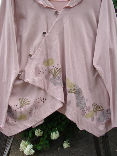 A pink shirt with a unique cross over tiny button wrap front, flowing feather weight batiste collar accent, and varying alternating hemline.
