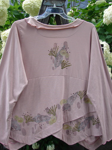 A pink shirt with a unique cross over tiny button wrap front, flowing featherweight batiste collar accent, and varying alternating hemline.
