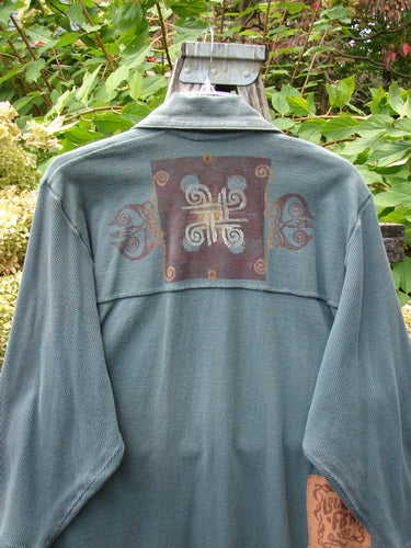 1996 Celtic Filias Jacket: A loose-fitting, slate-blue/teal jacket with a unique abstract yoke design, featuring drop shoulders and roomy sleeves, hangs outdoors, highlighting its distinctive style from BlueFishFinder.com.