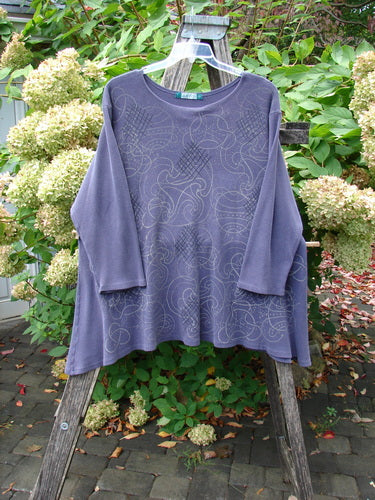 Barclay Thermal A Lined Top Spirograph Plum Size 2, showcasing a loose-fit, long-sleeved design with a sweeping hemline and subtle linear swirl pattern, elegantly displayed on a wooden stepladder outdoors.