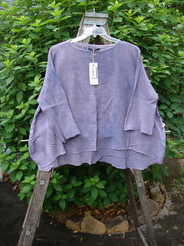 Barclay NWT Crinkle Gauze Crop Top Mottled Smokey Lilac OSFA displayed on a wooden ladder, showcasing its high-low hemline, three-quarter dolman sleeves, and soft texture.