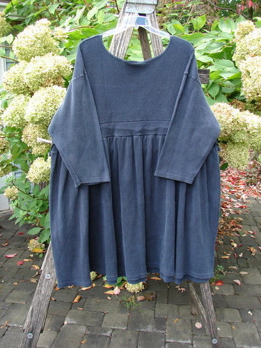 1992 Thermal Circus Dress Unpainted Black Size 2, featuring a loose fit with long sleeves and gathered empire waist, elegantly displayed on a wooden hanger amidst lush greenery, highlighting its unique vintage charm.