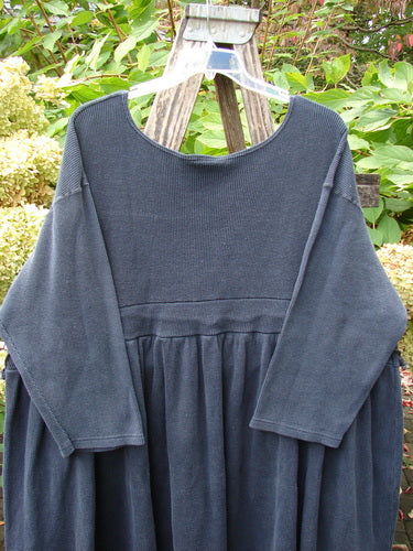 1992 Thermal Circus Dress Unpainted Black Size 2, featuring a wide scooped neckline and fitted bodice with a gathered skirt, displayed on a clear hanger against a lush garden backdrop.