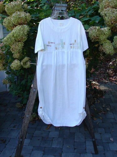 1999 Textured Linen Water Dress Tiny Fish White Size 0, featuring short sleeves, gathered waist, subtle chest embroidery, and dainty pleats, displayed on a wooden hanger against a patio backdrop with flowering shrubs.