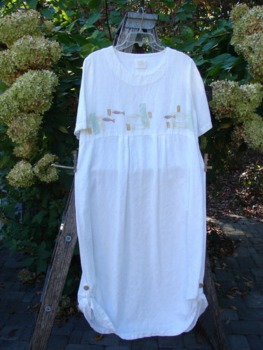 1999 Textured Linen Water Dress Tiny Fish White Size 0, featuring a round neckline, short sleeves, pastel embroidery, and a gathered hem with button tabs, displayed on a rustic ladder amidst garden blooms.