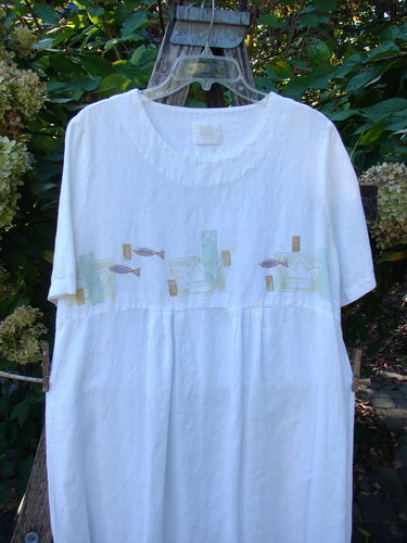 1999 Textured Linen Water Dress Tiny Fish White Size 0, featuring a loose fit, empire waistline, decorative band with fish motifs, and pleated front, hangs outdoors against hydrangea foliage.
