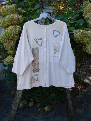 1995 Stargazer Jacket Chair Row China OSFA: Loose-fitting, light-colored cardigan with three-quarter sleeves, abstract geometric designs, single chest pocket, and original buttons, displayed on a wooden support with hydrangeas in the background.