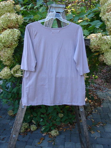 Barclay Three Quarter Sleeved Tee Play Dress Up Lilac Size 1, displayed on a wooden hanger against foliage, highlights its delicate neckline and three-quarter sleeves, crafted from organic cotton. Perfect for expressing individuality.