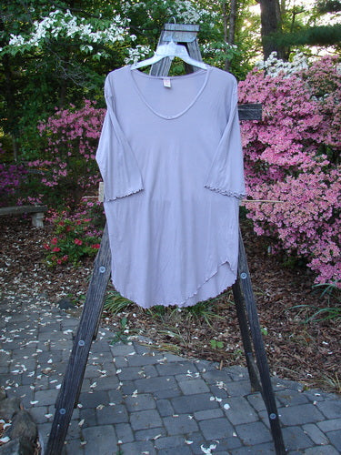 Barclay Batiste Round Bottom Shirt Unpainted Lavender Size 1 displayed on a wooden rack, showcasing its deep neckline, curly edgings, rounded hemline, and three-quarter length sleeves.